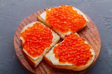 Bruschetta with red caviar on a wooden board on a gray background.