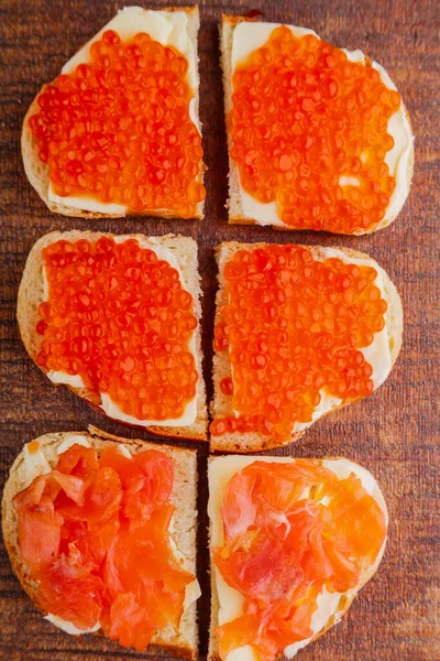 Bruschetta with red caviar and fish on a wooden board. — Foto Stock