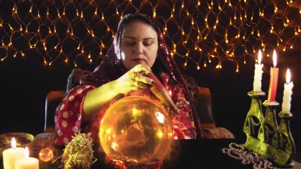 Woman fortune teller by candlelight reads the future in a crystal ball — стоковое видео