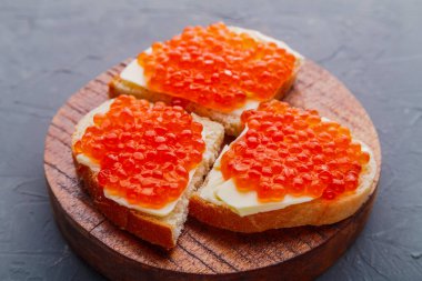 Bruschetta with red caviar on a wooden board on a gray background.