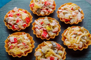 Salad with crab in tartlets on a black background close-up.