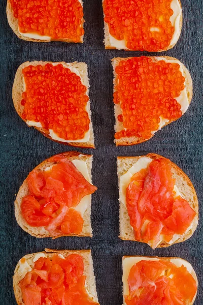 Bruschetta with trout and red caviar on a black board. — Stock Photo, Image