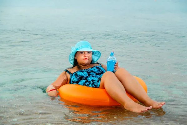 Een joodse vrouw met een strohoed en een bril in de zee in een zwemcirkel met een cocktail in haar hand. — Stockfoto