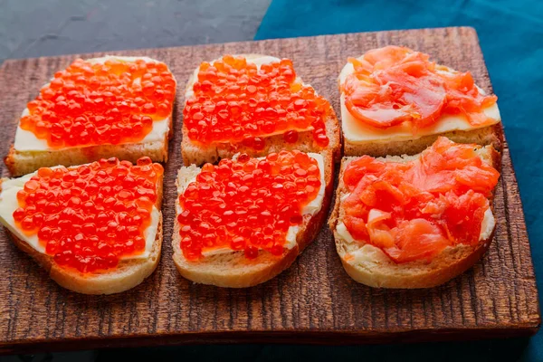 Bruschetta com caviar vermelho e peixe em uma tábua de madeira marrom. — Fotografia de Stock