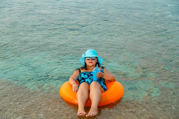 Hasır şapkalı ve gözlüklü Yahudi bir kadın elinde kokteyl ile yüzme çemberinde. Yatay fotoğraf
