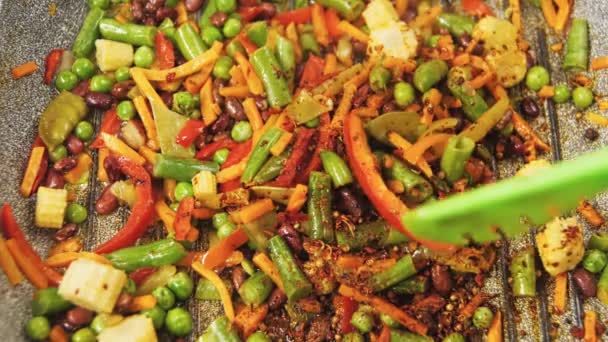 Zamrożone warzywa smażone na patelni w oleju miesza się z szczypcami. Powoli. — Wideo stockowe