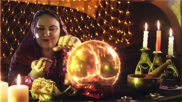 Uma jovem feiticeira está envolvida em magia, lendo o destino de uma pequena bola à luz de velas. — Vídeo de Stock