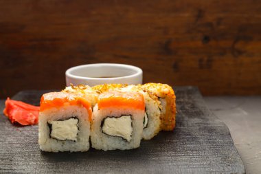 Soya sosunun yanında siyah bir tahtanın üzerinde yuvarlanıyor ve arka planda zencefil var. Yatay fotoğraf