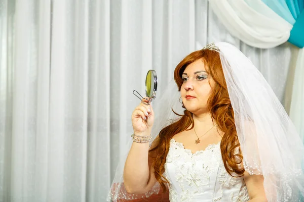 The sad Jewish Bride in the room before the Hupa ceremony in a wedding dress with a veil looks in the mirror to see if there are any tears. Horizontal photo
