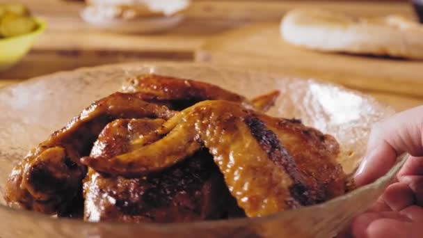 A womans hand puts a plate with grilled chicken wings on the table — Stock Video