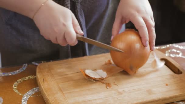 Μια γυναίκα χέρι με ένα μαχαίρι ξεφλουδίζει κρεμμύδια σε ένα ξύλο κοπής — Αρχείο Βίντεο