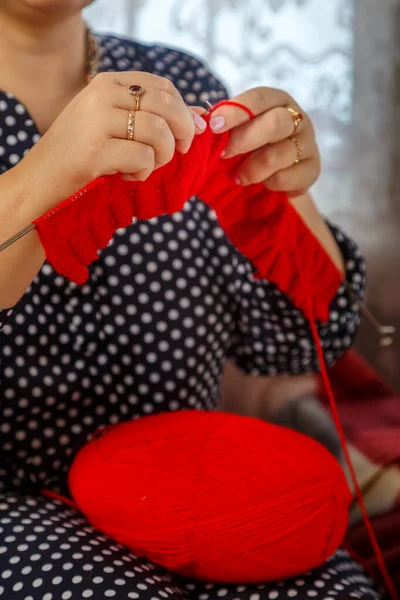 a woman without a face knits on knitting needles from red yarn. vertical photo