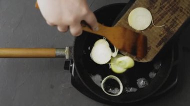 Spatulalı bir kadın eli, doğranmış soğan halkalarını yağlı tavaya döküyor..