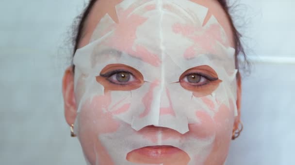 Une femme avec un masque en tissu sur son visage tapote son visage avec ses mains — Video