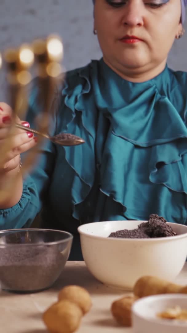 Вертикальное видео, где еврейка в головном уборе наливает маковые семена из ложки в миску для начинки гоменташа — стоковое видео