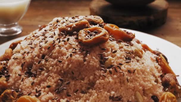 Vlaszaad wordt gegoten in een bord met couscous met gedroogde vruchten en noten — Stockvideo