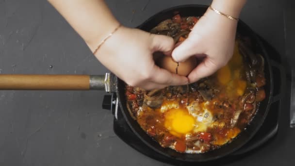 Kvinnors händer bryter ett ägg med en kniv och dumpar det i en stekpanna med shakshuka — Stockvideo