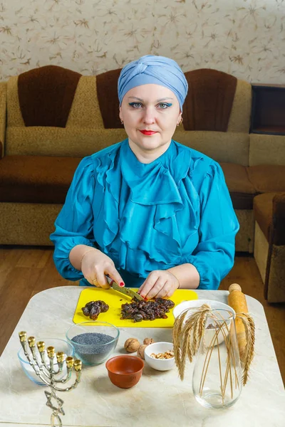 Еврейская женщина в традиционном головном уборе за столом, где есть менора, готовит начинку из семян мака и чернослива для печенья гоменташи в праздник Пурим. — стоковое фото