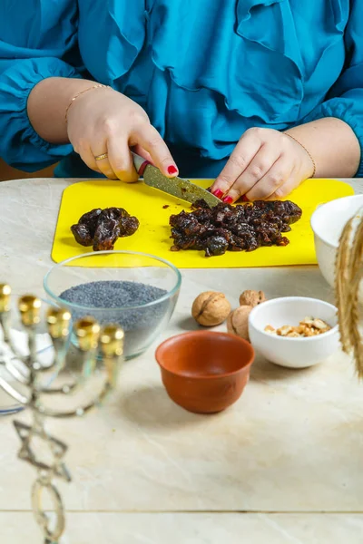 Женские руки делают чернослив для макового печенья гоменташи, традиционного для еврейского праздника Пурим, на столе, где есть менора. — стоковое фото