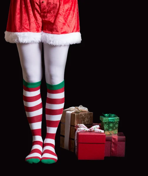 Santas Elf legs next to a pile of Christmas gifts over black Stock Picture