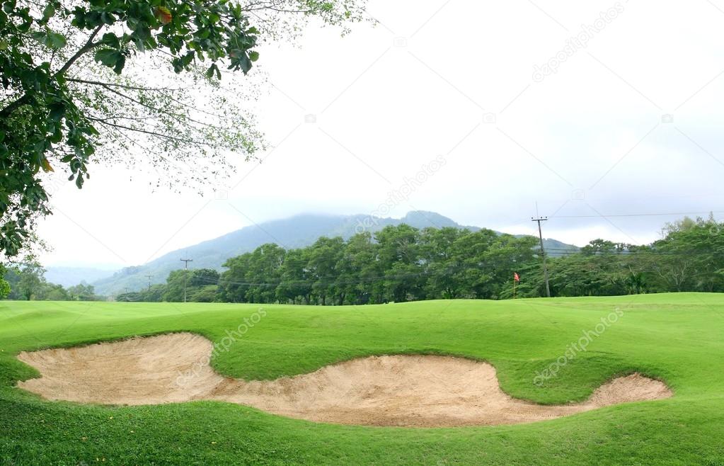 Sand bunker on the golf course with green grass and trees