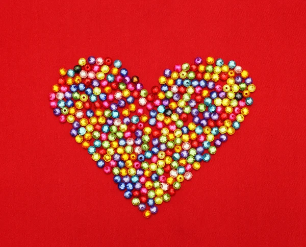Contas coloridas forma do coração isolado no fundo vermelho — Fotografia de Stock