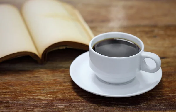 Kopje koffie met boek over een houten tafel — Stockfoto