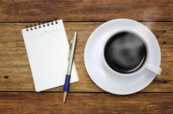 Koffie beker notebook en pen op de achtergrond houten tafel — Stockfoto