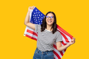 Sarı arka planda Amerikan bayrağı taşıyan neşeli etnik kökenli genç bir kadın.