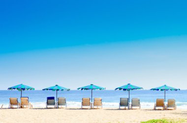 Plaj sandalyeleri ve kumsalda şemsiyeyle