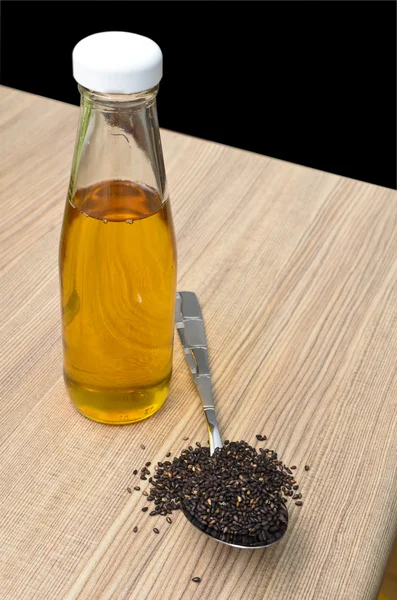 Sesamöl in der Flasche und schwarzer Sesam im Löffel auf Holz — Stockfoto