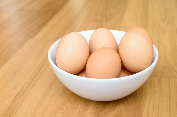 Eieren in witte kom op houten tafel — Stockfoto