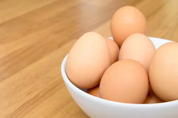 Eier in weißer Schüssel auf Holztisch — Stockfoto