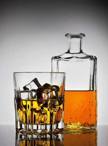 Faceted glass of whiskey with ice and a bottle — Stock Photo, Image