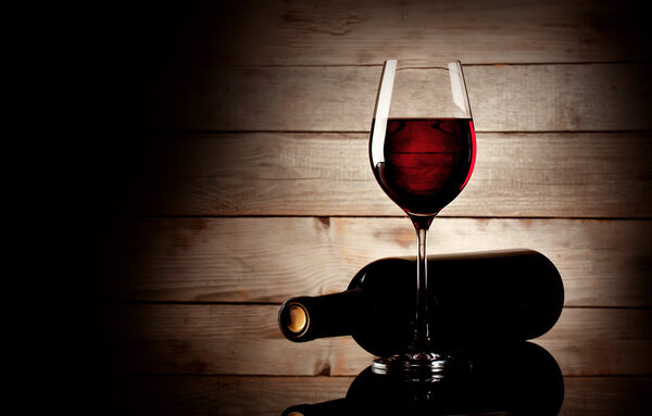 Бокал красного вина и бутылка, лежащая на боку
