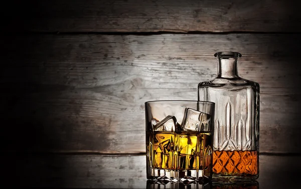 Glas whiskey med isbitar och facetterade flaska — Stockfoto