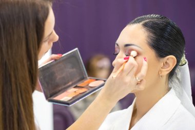 Makyaj sanatçısı elinde kozmetik seti olan güzel bir kıza makyaj uygular.