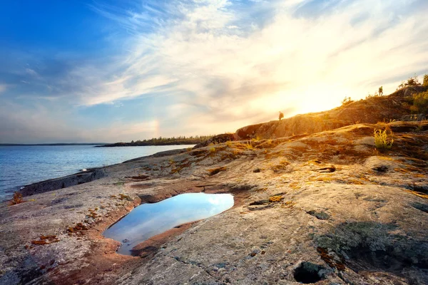 Rotsachtige oever van het meer met plas reflecterende hemel — Stockfoto