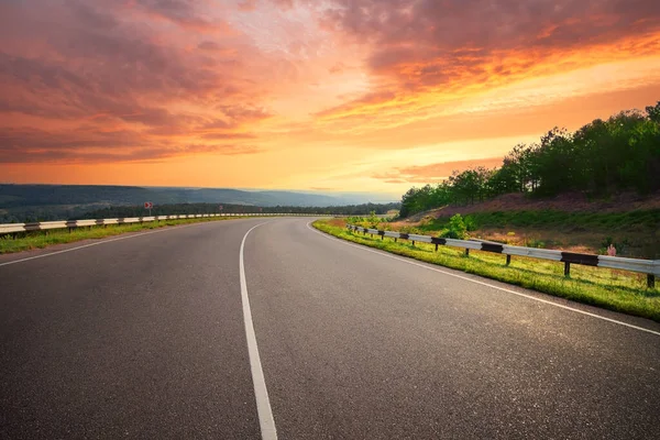 Curvando estrada de asfalto sob céu pôr-do-sol dramático — Fotografia de Stock