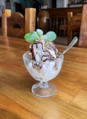 Çikolata kaplı bir kasede dondurma ve ahşap bir masada nane yaprakları.
