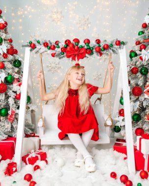 Güzel sarışın kız Noel 'i kutluyor. Yeni yıl havası. Noel süslemeleri olan kırmızı elbiseli küçük bir kız. Hediyeler