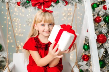 Güzel sarışın kız Noel 'i kutluyor. Yeni yıl havası. Noel süslemeleri olan kırmızı elbiseli küçük bir kız. Hediyeler