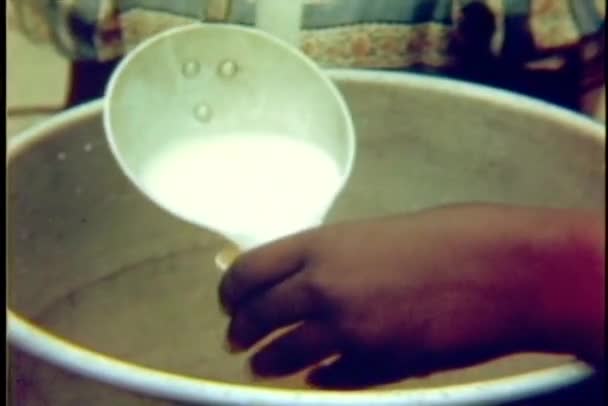 Μεγέθυνση της χέρια ρίχνει το γάλα από την κουτάλα για να πλαστικό κύπελλο και μοιράζουν ψωμί — Αρχείο Βίντεο