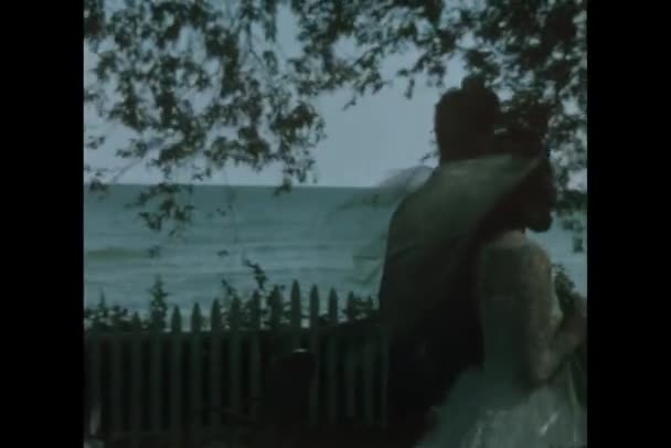 Вид сзади на молодоженов, прогуливающихся во дворе пляжного домика — стоковое видео