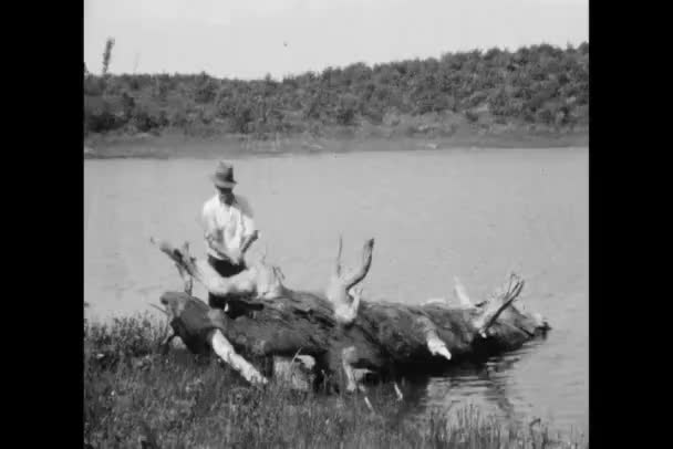 Wide shot of man chopping wood by lake — Stock Video