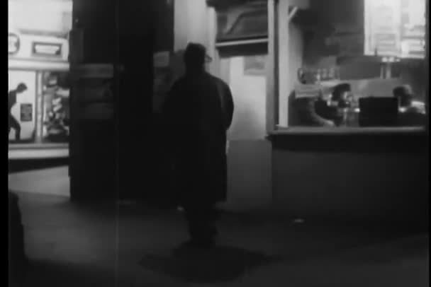 Мужчина в длинном пальто ходит по городской улице ночью — стоковое видео