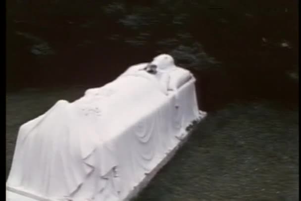 Grafsteen in de vorm van een vrouw slapen op een bed houden van bloemen — Stockvideo