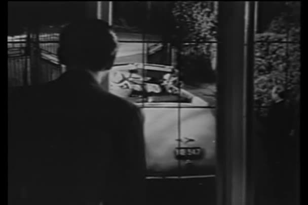 Мужчина смотрит в окно на людей, уходящих в машине — стоковое видео