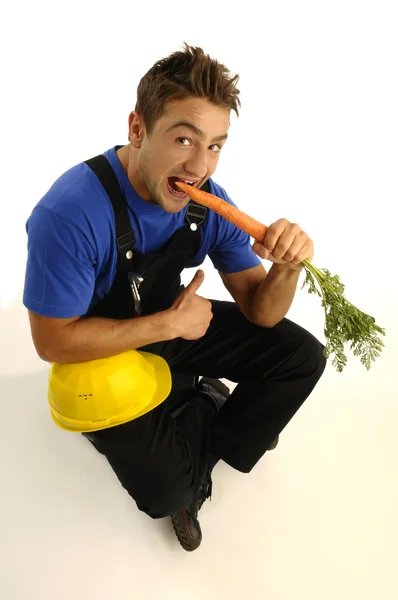 Jovem trabalhador comer cenoura — Fotografia de Stock