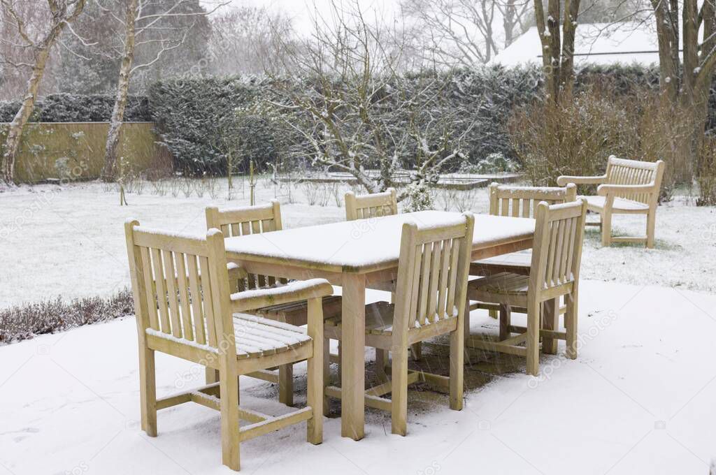 Patio garden furniture, wooden table and chairs covered with snow in winter, UK